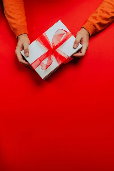 Man in cozy red sweater holding beautiful Christmas gift box, present with red ribbon.Happy surprise.Merry Christmas.Red background, birthday presents. Copy space for text, banner or card. Vertical