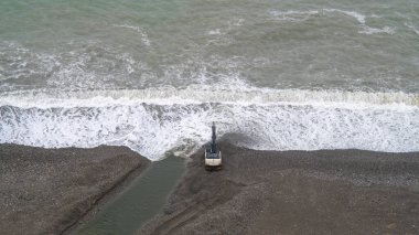 Kazı makinesi, yağmurlu bir havada denizde fırtına sırasında kumsalda çalışır. İnşaat ve yeniden yapılanma