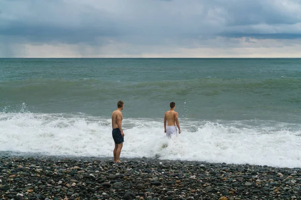 Due Giovani Uomini Camminano Mare Schiuma Sulla Spiaggia Durante Una — Foto Stock