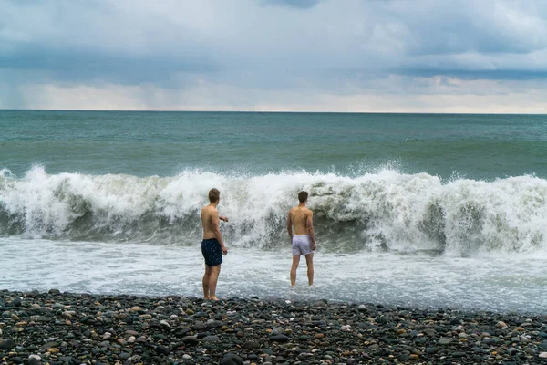 Due Giovani Uomini Camminano Mare Schiuma Sulla Spiaggia Durante Una — Foto Stock
