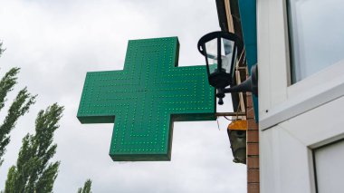 Bulutlu bir arka planda, eczanenin yanındaki yeşil haç.