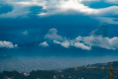 Şiddetli yağmur bulutları şehrin üzerinde ve dağlarda yağmurlu bir yaz sabahı, ön planda sağ köşede bir inşaat vincinin jeti var.