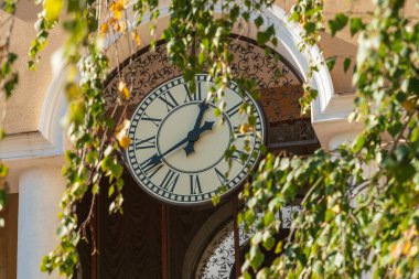 Ekim ayında güneşli bir günde sonbahar yapraklarının arkasındaki sokak saati. Sonbahar başlama zamanı