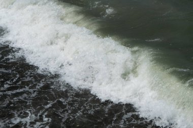 Deniz dalgaları kıyıya yakın güneş ışınlarında köpürüyor.