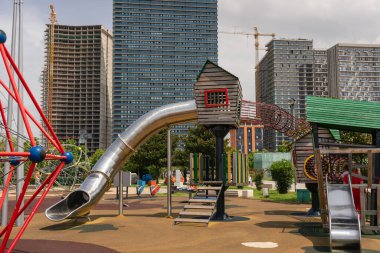 Güneşli bir yaz gününde, şehir parkındaki bir oyun parkındaki oyuncak ahşap bir ev büyük şehir gökdelenlerinin ve gökyüzünün zeminine karşı.