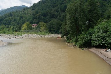 Bir grup insanla birlikte bir dağ nehrinde yüzen şişme bir tekne. Kıyısında güneşli bir dağ plajında güneşlenen bir adam.
