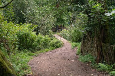 Tahta bir köprünün karşısındaki dağ yolu, arka plandaki bir ağacın gölgesinde bir ağaç standının arkasında oturan bir sokak şarap satıcısına çıkar.