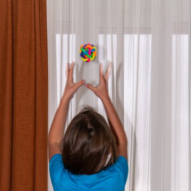 Bir kız evin önünde küçük renkli bir top atar ve yakalar.