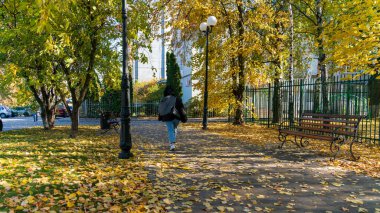Bir kadın, bir sonbahar gününde bir şehir caddesinde düşen sonbahar yaprakları üzerinde hızla yürür.