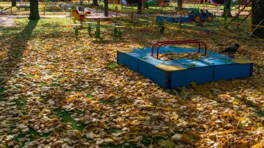 Oyun parkında sonbahar yaprakları, düşen yapraklarda ışık ve gölge oyunları ve çok renkli oyun alanı tasarımları.