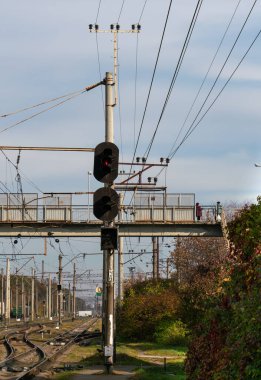 Demiryolu üzerindeki yaya köprüsünün yanındaki güneşli bir sonbahar gününde, tren yolu trafik ışıklarında sarı ışık. Demiryolu taşımacılığı ve seyahat