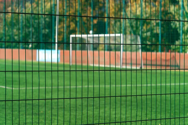 Bir futbol stadyumunun metal örgüsü güneşli bir sonbahar gününde kapanıyor ve arka planda bir futbol golü var.