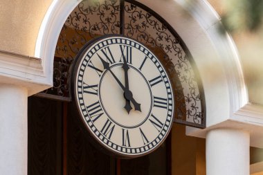 Saatin elleri, sarı duvardaki saatin büyük beyaz kadranında 12 'ye 7 kala.