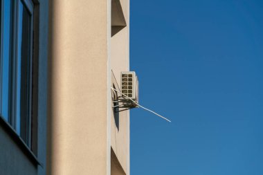 Şeftali rengi bir duvarda klima ve mavi gökyüzünün arka planında pencereler. Modern mimarinin evlerinin cephelerinde klimalar var.
