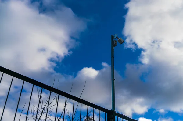 户外的监控摄像头在一个金属栅栏上 背景是蓝天白云 城市安全 — 图库照片
