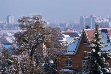Ağaçların dallarındaki beyaz kar ve evlerin çatıları kış güneşli bir günde gökyüzünün altında.