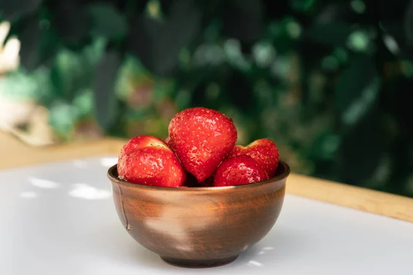 Strawberry dessert. A strawberry poured with honey stands on a white table in the shade of a cherry. Sun rays fall through green leaves on red strawberries