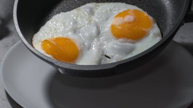 Kahvaltı için indüksiyon sobasında çırpılmış yumurta pişirmek için metal bir tavanın sıcak ve yapışmaz yüzeyinde iki yumurta üzerinde.