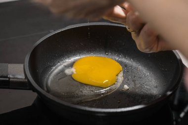 Dişi bir tencere içinde yumurta uzatıyor, tencerenin siyah yüzeyinde, çırpılmış yumurta pişiriyor.