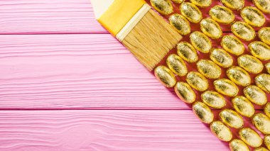 Sarı boya fırçası, çikolatalı yumurta, altın folyo, pembe ahşap masa, paskalya kartı için arka plan.