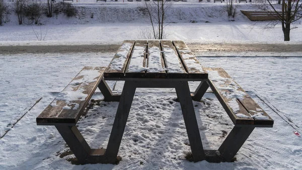 Tahta masa ve ahşap banklar güneşli bir kış gününde şehir parkında buzla kaplı bir gölün kıyısında.