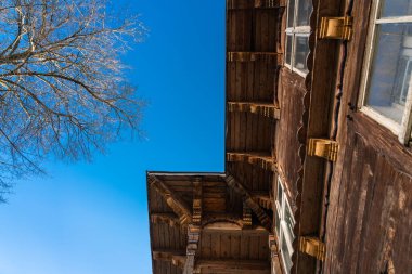 Yapraksız bir ağacın tacı akşam güneşinin ışınlarında eski binanın ahşap duvarına karşı kış akşamının erken saatlerinde mavi gökyüzüne karşı. Alt görünüm