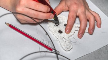 Küçük bir kızın eli kırmızı bir 3D basım kalemi tutuyor ve masanın üzerinde bir Paskalya tavşanı burnu, kırmızı bir kalem ve siyah bir iplik yapıyor. Üst taraf görünümü