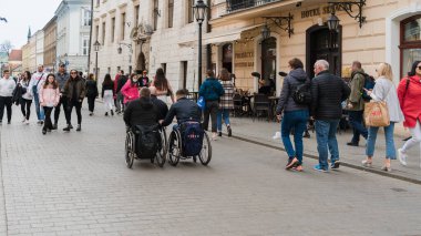 Polonya, Krakow, Mart 2022: Tekerlekli sandalyeli üç engelli, onlara bakan sağlıklı insanlar arasında bir şehir caddesinde birlikte yolculuk ediyor. Engelli insanların topluma entegrasyonu