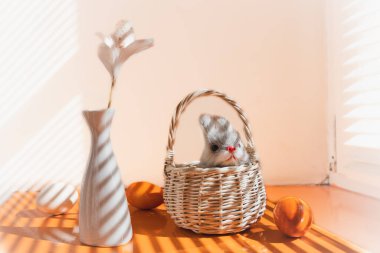 Turuncu bir yüzey üzerindeki mutlu bir Paskalya bayramının özellikleri. Panjurlardan süzülen ışık çizgileri. Turuncu yumurtalar, sepette bir tavşan, beyaz vazodaki bir bıldırcın yumurtası.