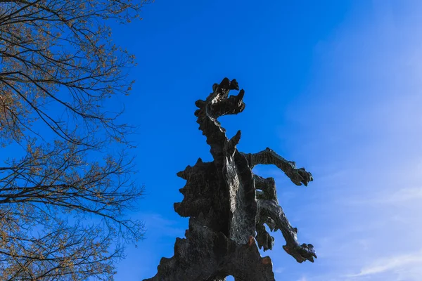 Wawel ejderhası, Polonya 'nın Krakow şehrinde güneşli bir günde mavi gökyüzüne karşı ağaç dallarının arkasında.