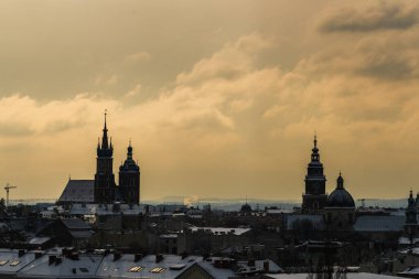 Eski Krakow 'un şafak vakti St. Mary Bazilikası ve Belediye Binası Kulesi ile şehrin ortaçağ ana pazar meydanında hava manzarası, Polonya' nın bulutlu havasında Krakow evlerinin çatılarında kar