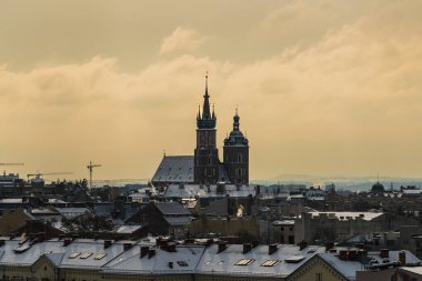 Eski Krakow 'un şafak vakti St. Mary Bazilikası ile şehrin orta çağ pazar meydanında hava manzarası bulutlu havalarda Krakow evlerinin çatılarında kar.