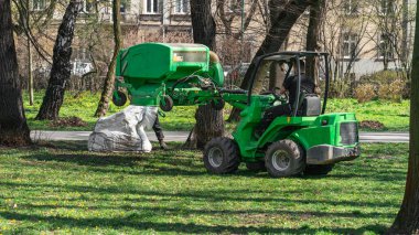Bir belediye çalışanı, Krakow 'daki şehir parkının yeşil çimlerini bahar başında belediye aracıyla eski yapraklar ve dallardan temizliyor.