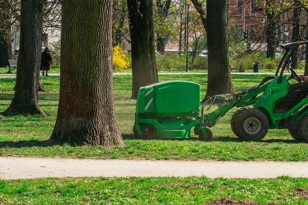 Belediye arabası nisan ayında güneşli bir günde, Krakow 'daki şehir parkının yeşil çimlerini eski yapraklardan ve dallardan temizler.