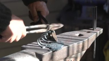 Büyük maşaları olan isimsiz bir demirci, bir örs, yakın plan aletler ve metal bir parçayla sıcak metal bir askıyla çalışır. Nadir meslekler, geleneksel demircilik.