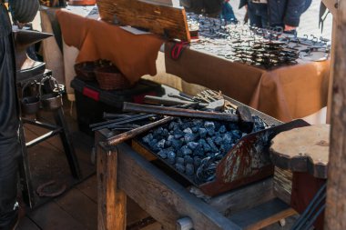 Demirci aletleri, modern dünyada adil, eski bir meslekte ve el işçiliğinde güneş ışığında dövülmüş metal ürünleri olan tezgahın arkasındaki siyah kömürün üzerinde yatıyor.