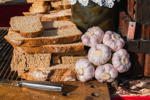 Close-up of a head of garlic, slices of sliced fresh bread, a glass jar of pickled cucumbers in the sun under the open sky on the counter of a food festival in Krakow. Traditional Polish cuisine