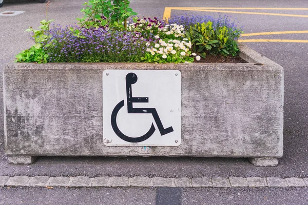 Disabled parking sign on a concrete box with blooming flowers in an open street parking lot in Liechtenstein\'s capital Vaduz, caring for people with disabilities