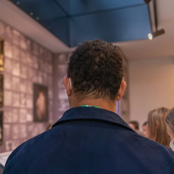 An ethnic man next to a European woman in a medical mask listens to a guide in a museum in a mixed age group of tourists, ethnic diversity and tolerance in European cities