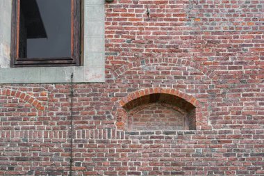 Ortaçağ penceresinin tıkanmış bir oyuğu ve camda yansımaları olan büyük bir penceresi olan eski, kırmızı tuğla bir binanın eski duvarı.