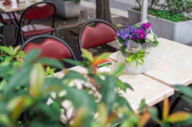 Sabahın erken saatlerinde bir yaz kafesinin masasında çiçekler, kırmızı derili metal sandalyeler, şehirde hızlı bir kahvaltı.