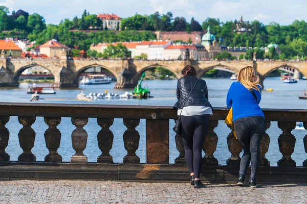 Çek Cumhuriyeti 'nin Prag kentindeki Charles Köprüsü' nün taştan korkuluklarında güneşli bir günde Vltava nehri ve eski kasabanın manzarasına hayran olan iki turist Avrupa 'ya seyahat ediyor.