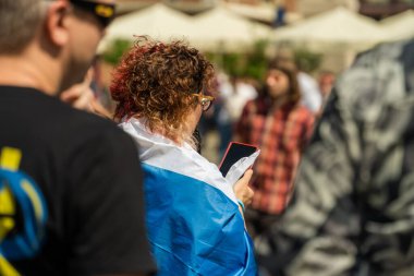 Güneşli bir günde elinde telefonla beyaz-mavi-beyaz bir bayrak taşıyan bir Rus aktivist, Rusya 'nın Ukrayna' yı işgaline karşı Avrupa 'da bir savaş karşıtı protestoya katılıyor.