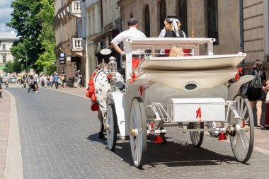Güneşli bir yaz gününde eski bir Avrupa şehrinin taşlı yolunda turistlerle dolu beyaz at arabası, modern Avrupa şehirlerinde geçmişten kalma sürdürülebilir bir araç.