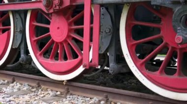 Paslı metal rayların üzerinde buharlı lokomotifin beyaz kenarlı çelik kırmızı tekerlekler. Geçmişin ulaşımı, zaman döngüsü. Yakın plan.
