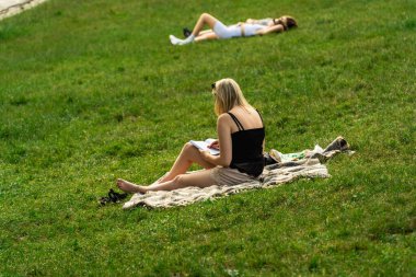 Genç bir kız çıplak ayakla güneşli bir günde yeşil çimlerin üzerinde kitap okuyor, bir kız öğrenci boş zamanlarında halka açık bir parkta kendi kendini eğitiyor, yazları yeşil çimlerin üzerinde sarışın bir kadın.