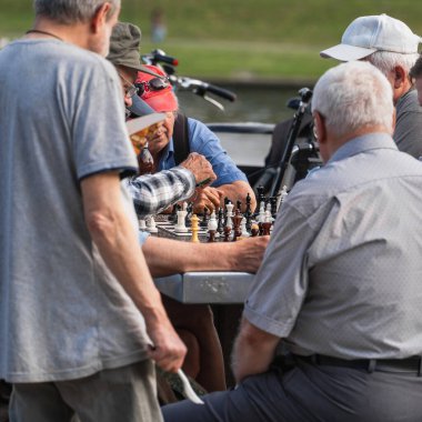 Chess board with wooden chess pieces on a concrete street table, elderly men play chess on the street of Krakow, outdoor board game, chess duel on a summer day, pensioners sports games