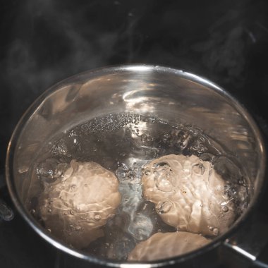 Metal bir tavada haşlanmış yumurtalar, tavuk yumurtasıyla kaynar su içerken köpükler ve buhar. Hızlı kahvaltı.