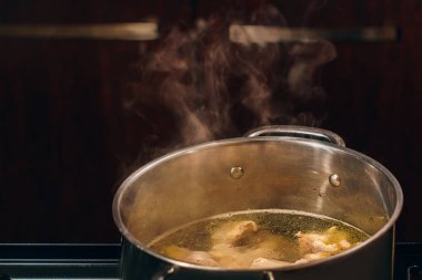 Close-up of broth in a steel saucepan on the stove, pieces of white chicken meat are boiled in a saucepan, hot meat broth for soup. Top view, copy space
