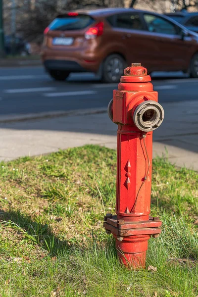 A red fire hydrant on the side of a city road on a sunny day in Krakow. Polish fire hydrant, vertical orientation